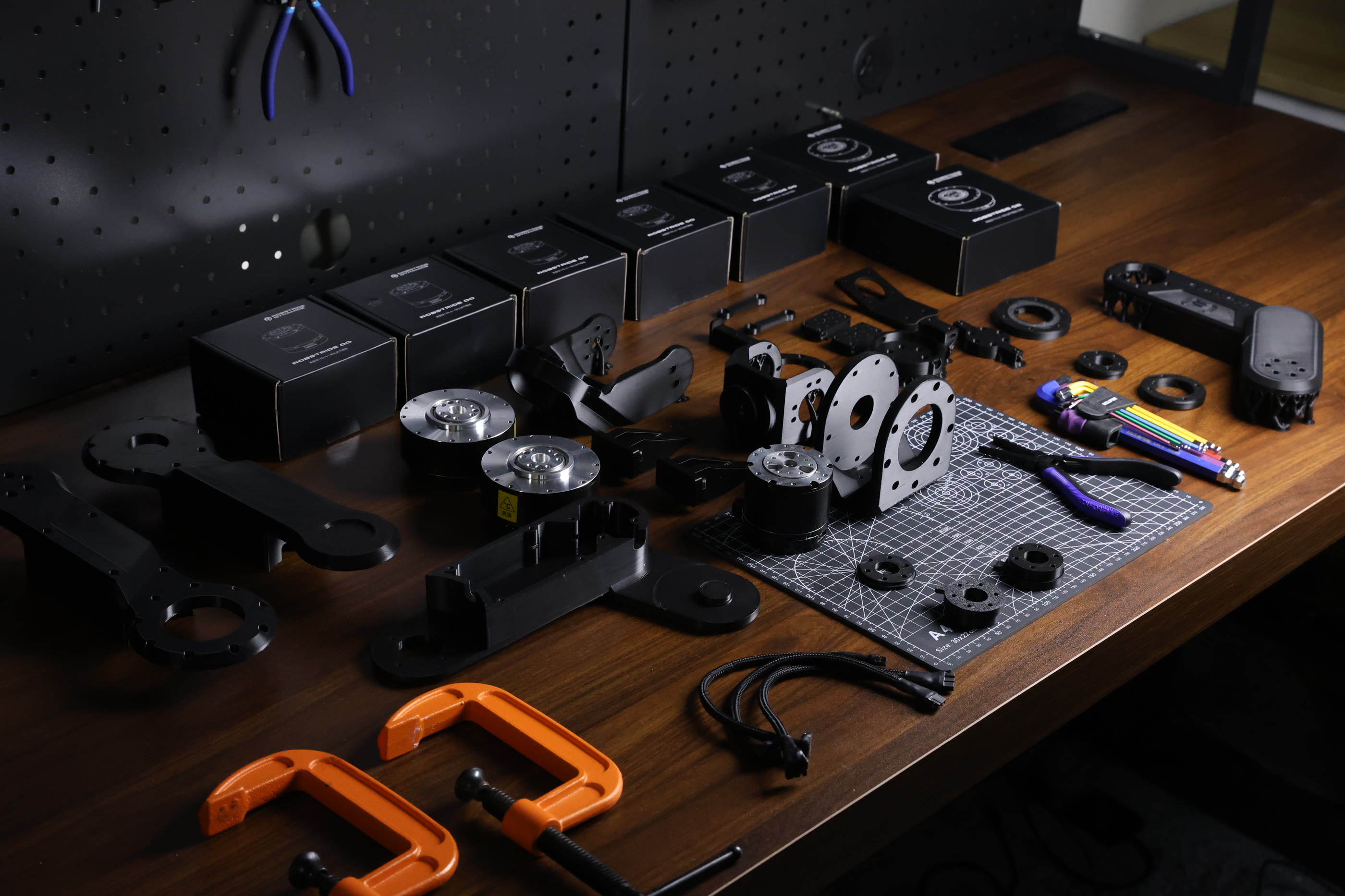 Maker Arm kit laid out on a bench: 3D-printed structural parts, boxed RobStride actuators, bearings, hardware, and cabling