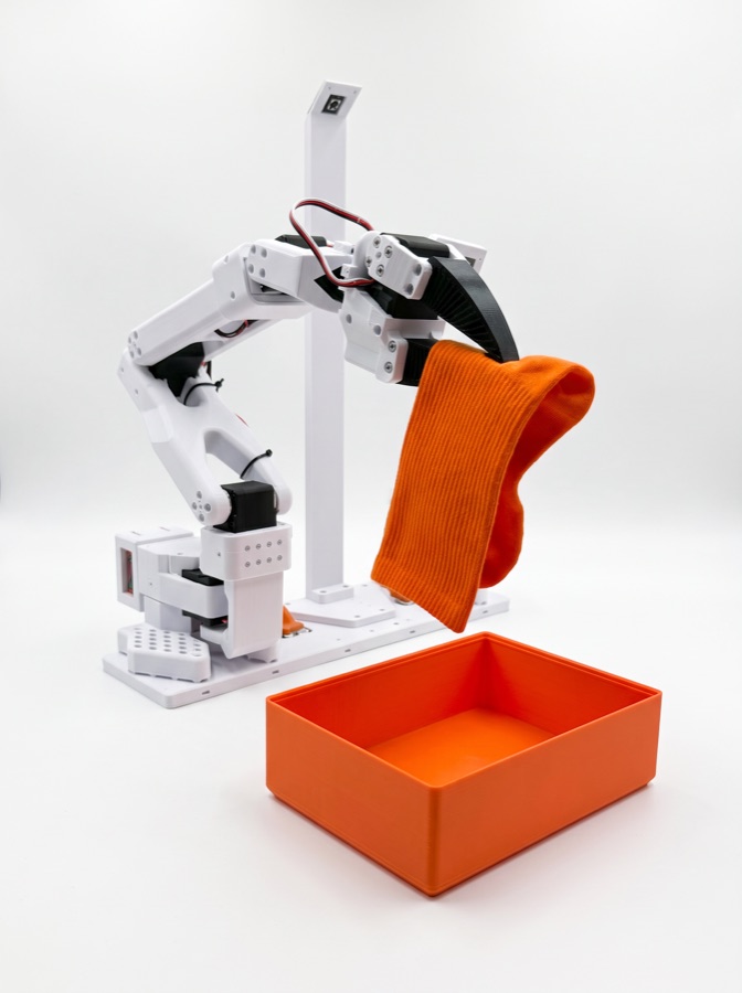 SO-101 robot sorting an orange sock into a tray